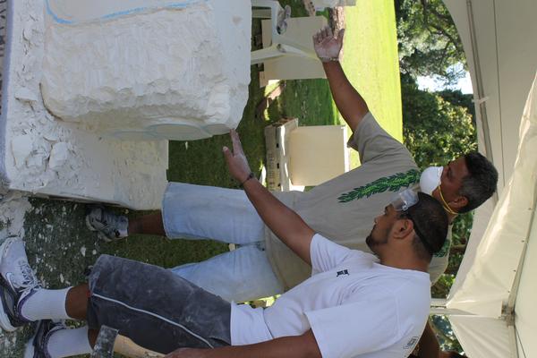 Master carver Filipe Tohi assists emerging artist Allen Vili with his carving